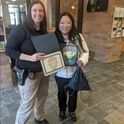 Officer standing next to a female who is holding a coloring contest sheet in the police lobby