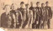 Old newspaper picture of seven male officers and one female office staff standing in a line. 