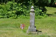 Trott Brook Cemetery, summer, old obelisk headstone, shrubs behind, pinwheel in ground on left