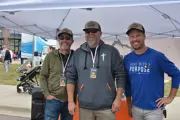 Three tall Caucasian men standing next to each other with big smiles on their faces under a canopy