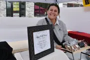 Caucasian woman with hands on a small shelf holding bagged baked goods, under a canopy