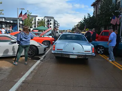 The back of an early 1980s Lincoln Continental driving through cars on either side as people watch
