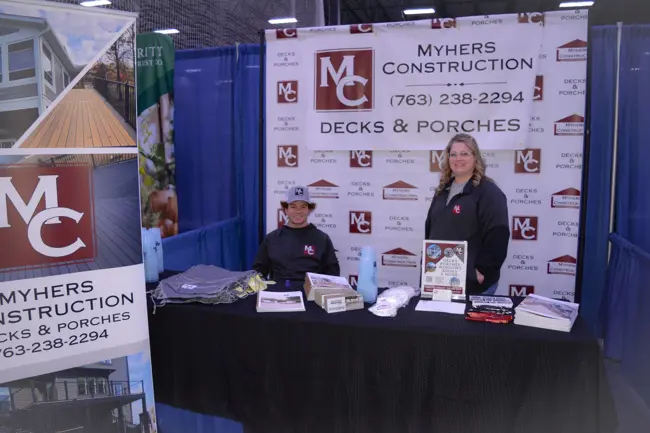 Man and woman smiling at Myhers Construction decks & porches booth with branded banner.