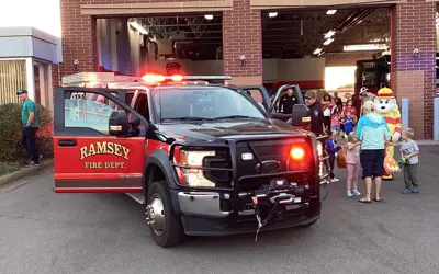 Smaller Fire Rescue truck in front of a fire House, community members looking at it