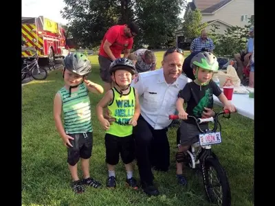Left two small Caucasian boys in bike helmets, firefighter kneeling, boy on a bike with helmet
