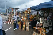 Older Caucasian woman stand in front of homemade interior decor, such as signs, artificial flowers, 