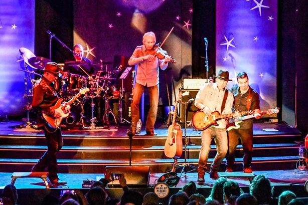 Five male band members performing from a stage in front of an audience