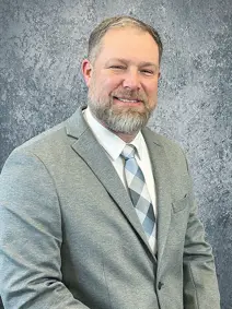 Council member Eric Peters has a beard with cropped hair, is wearing a suit and tie