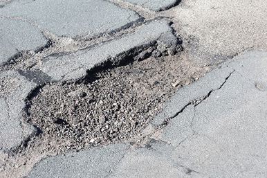 Pavement surface with a deep pothole in it with loose rock debris at the bottom of the hole