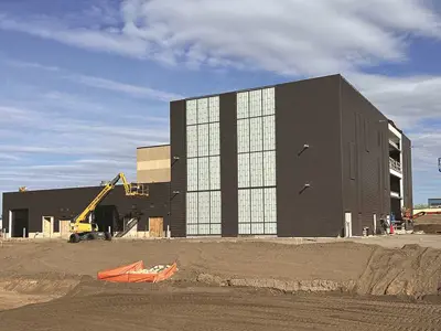 3 story large square building with opaque window panels down center, construction site, sunny sky