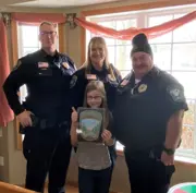 Three officers standing behind a child who is holding a coloring contest sheet. 