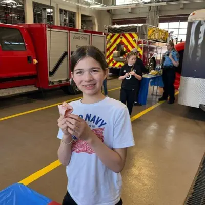 Child in fire station holding a piece of sandwich meat.