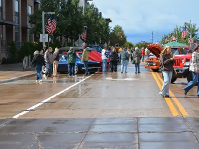 Car show crowd walking through class and late model cars on a wet street with ominous clouds in sky