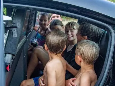7 wet children, 5 are sitting in the back of a police squad car during night to unite