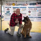 Older man holding a trophy kneeling next to his sitting German Shepard