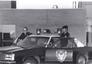 1970s, two officers standing next to the doors of a police car. 
