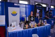 Woman smiling behind Summer Lakes Beverage booth with cocktail mix display at indoor expo.