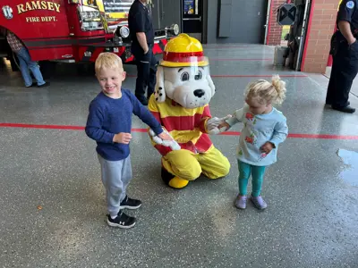 Two small children, boy left, girl right, high fiving Sparky the Fire Dog Mascot