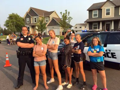 Police officer and six teenagers posing in front of a police car on a warm summer night. 