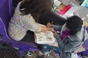Woman painting a Henna Tattoo design on a teenage girl's wrist, while sitting in folding chairs