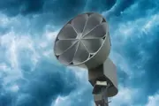 Outdoor warning siren shaped like a megaphone on a pole with angry clouds in the background