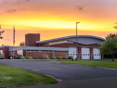 At sunset, left side lower flat roofed brick, right side 2 story 3 overhead doors, rounded roof