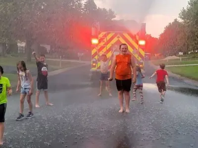 Fire truck in the middle of a residential street, 7 children playing a water spray 
