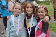 Three smiling little girls with their arms around each other at the 2025 Fun Run