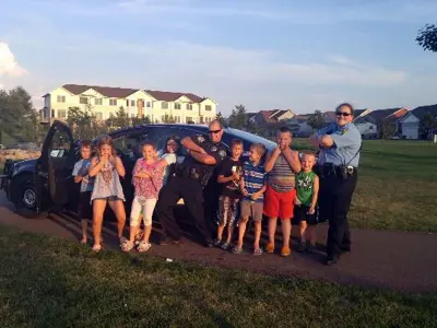 Police officer posing with four small children on both sides and a community service officer on end.