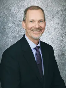 Council member Michael Olson, smiling has higher hair line, wearing a suit and tie