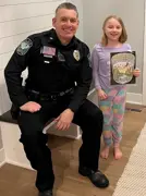 Officer siting on a bench next to a small child who is holding a coloring contest sheet.