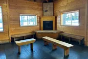 Room with tongue and groove pine walls stone corner fireplace with two benches in front