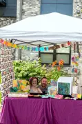 A man and woman sitting at a table in the vendor booth showcasing their paintings