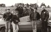 three males standing inside a car, three male and the former police chief standing in front of it.
