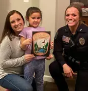 An officer and mother knelling next to a small child who is holding a coloring contest sheet.