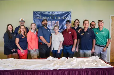 Group of men and women in front of RM Golf Business of Year banner white table in front.