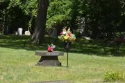 Trott Brook Cemetery in the summer, mid-sized granite headstone, flower bouquet next to it