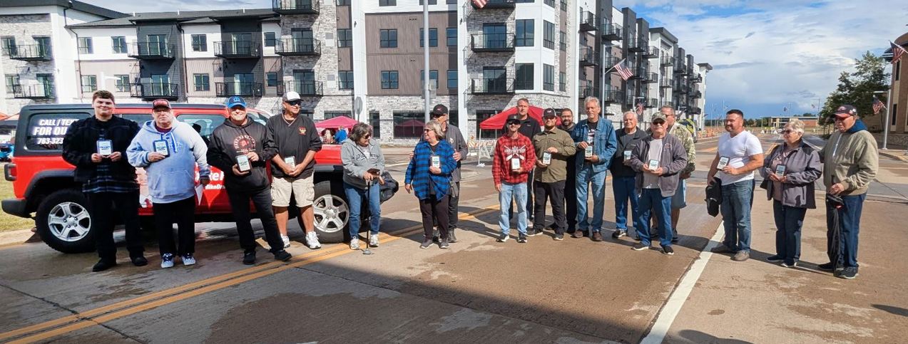 Line up of 16 male and female car show winners standing in the middle of an asphalt street