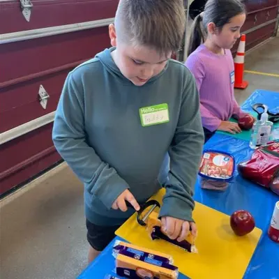 Child slicing cheese on a cutting board. 