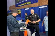 Man in hat interacting with smiling police officer at community expo booth.