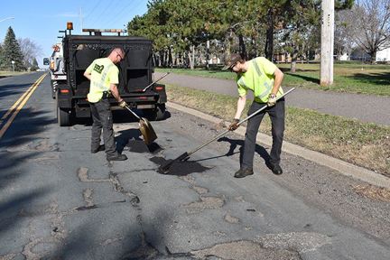 Two male city workers shoveling pavement patching materials in potholes and compacting it