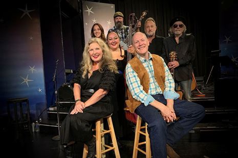 Three women and four men, staggered in three rows, some are holding instruments