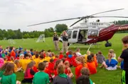 State trooper helicopter on a soccer field two troopers in front with many kids sitting in the grass