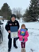 Officer standing next to a small girl while holding a coloring contest sheet while outside. 