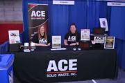 ACE Solid Waste staff at expo booth with giveaway items, signage, and recycling info.