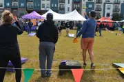 A woman and two men Cornhole Players from behind, man on right throwing a bag in the air 
