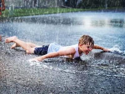 Child laying on their stomach on on the wet ground playing in water spray