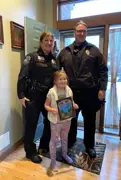 Two police officers standing in an entryway with a small child holding a coloring contest sheet. 