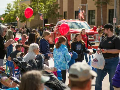 Happy Days parade route, people holding balloons and sitting in lawn chairs watch floats